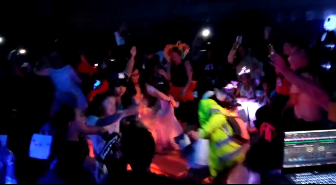 Students on a packed dance floor at a school event with colorful lighting and the DJ booth in the foreground