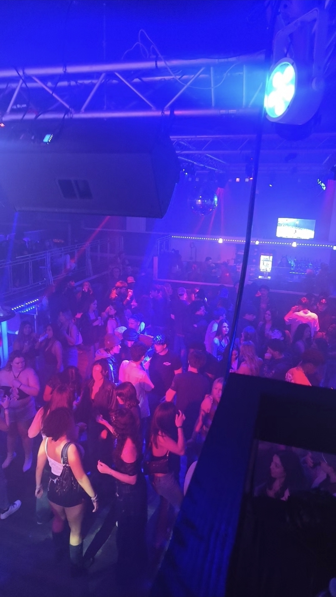 Packed nightclub dance floor lit in blue with disco ball