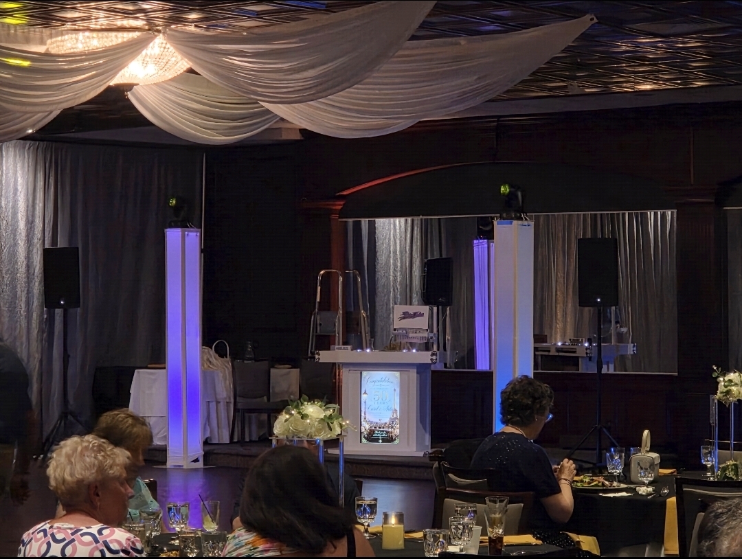 Guests dining at an anniversary celebration with a personalized Paris-themed 50th anniversary display and blue uplit dance floor in the background