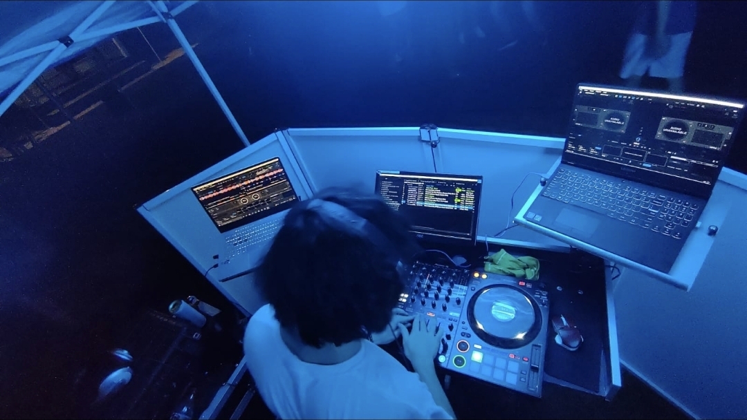Overhead view of DJ mixing on illuminated equipment under blue lighting at an outdoor tented private event