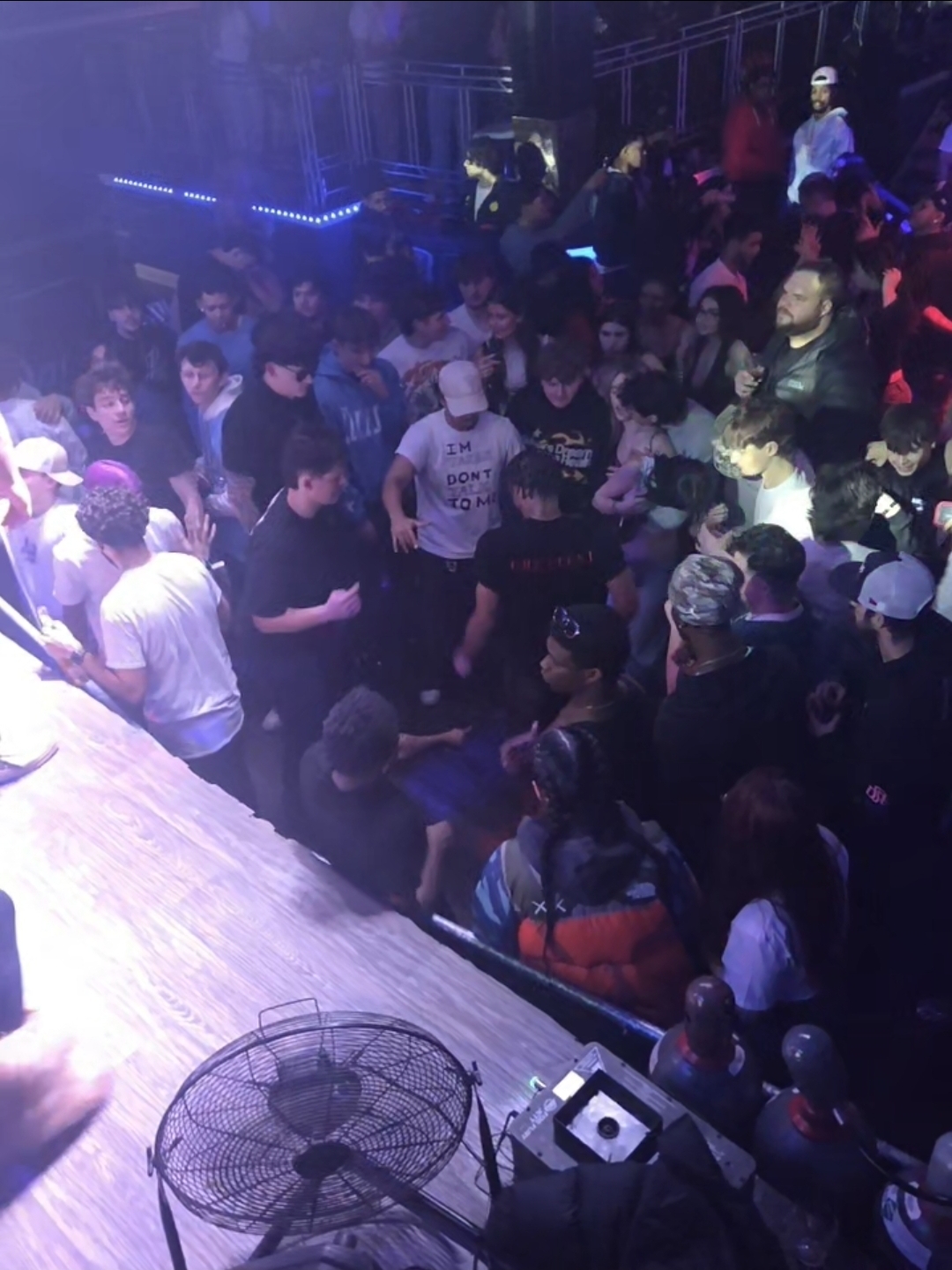 High-energy nightclub crowd gathered near the DJ booth under club lighting