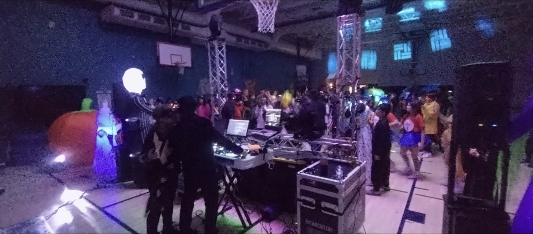 DJ Aiden Jules performing at a school event with a truss lighting rig and a full dance floor in a gymnasium